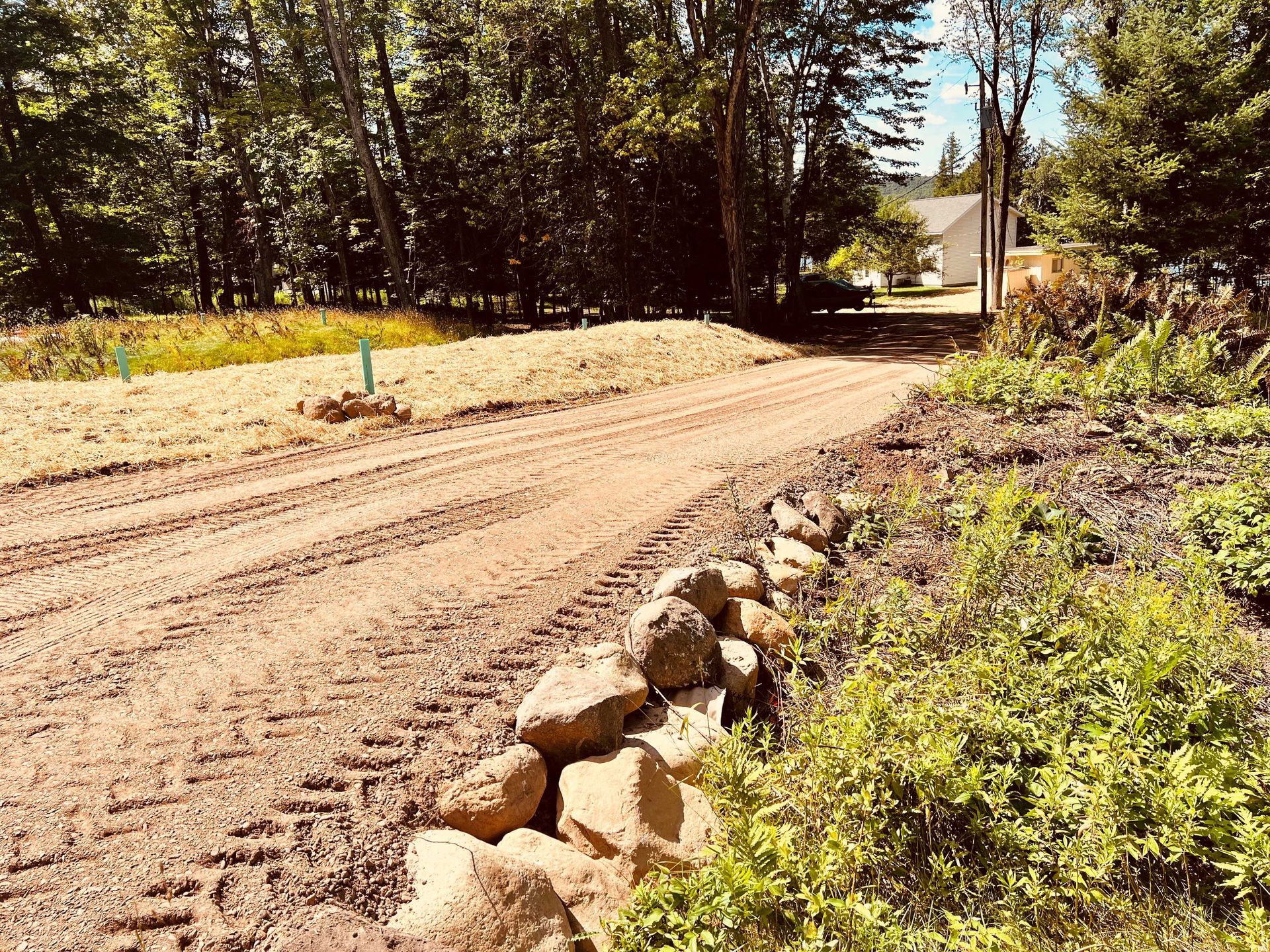 A dirt driveway with tire tracks, bordered by a stone wall on the right and a grassy bank on the left, leading to a house. A dirt driveway with tire tracks, bordered by a stone wall on the right and a grassy bank on the left, leading to a house.