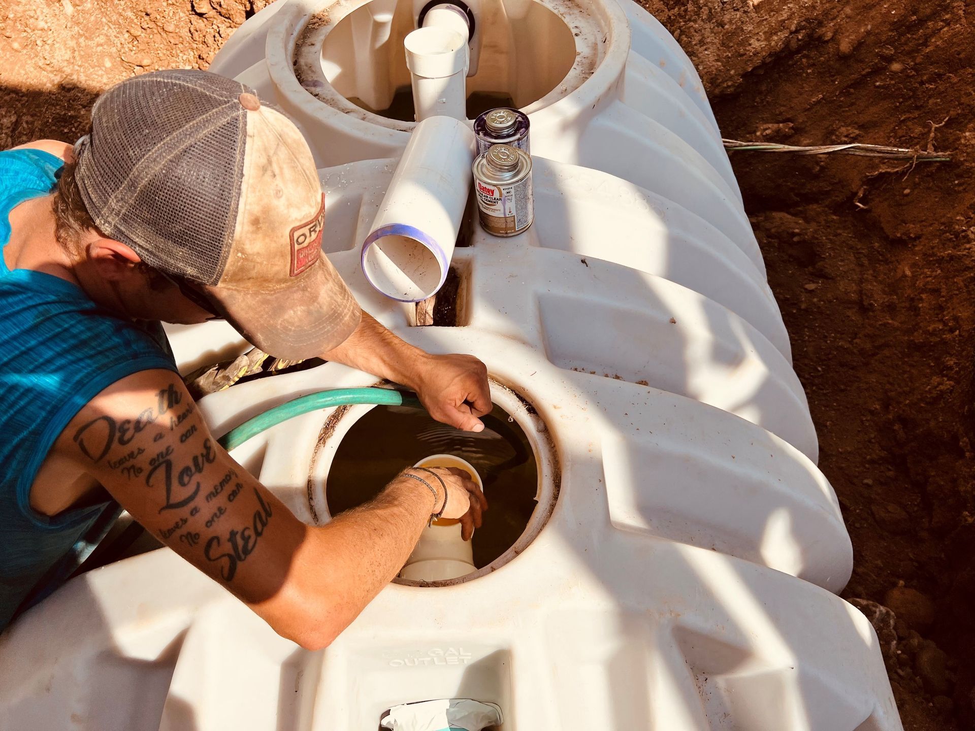 A person with a tattoo on their arm works on the piping inside an open plastic septic tank at a construction site. A person with a tattoo on their arm works on the piping inside an open plastic septic tank at a construction site.