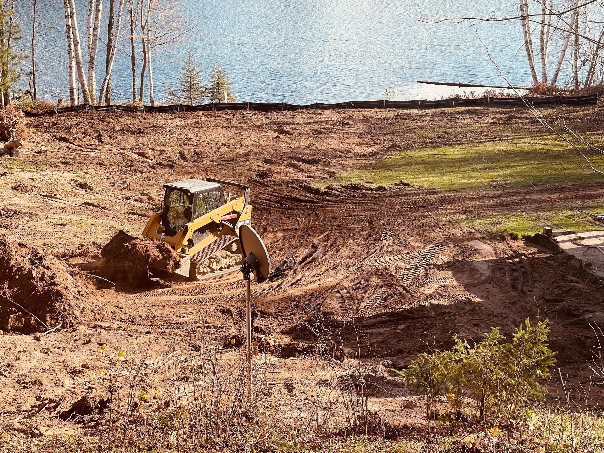 A yellow bulldozer clears dirt on a construction site overlooking a lake near trees.