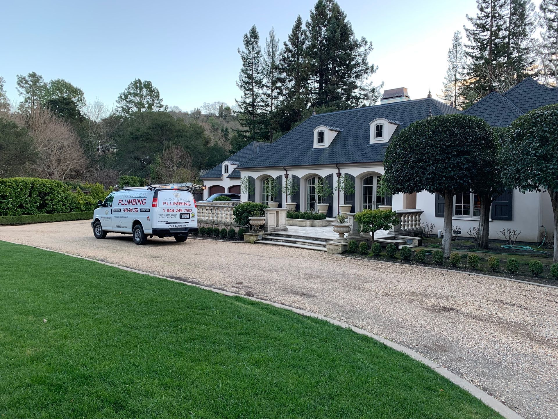 White house with blue roof on gravel driveway, a white work van parked outside, green lawn in front.