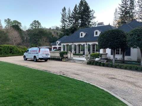 White house with blue roof on gravel driveway, a white work van parked outside, green lawn in front.