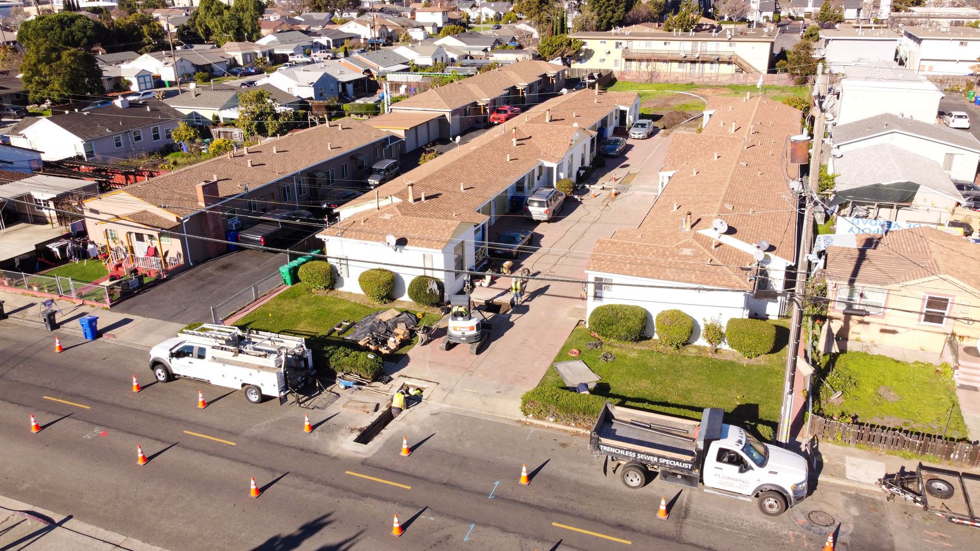 Aerial view of a residential street with houses, parked trucks, and construction work on rooftops and driveways