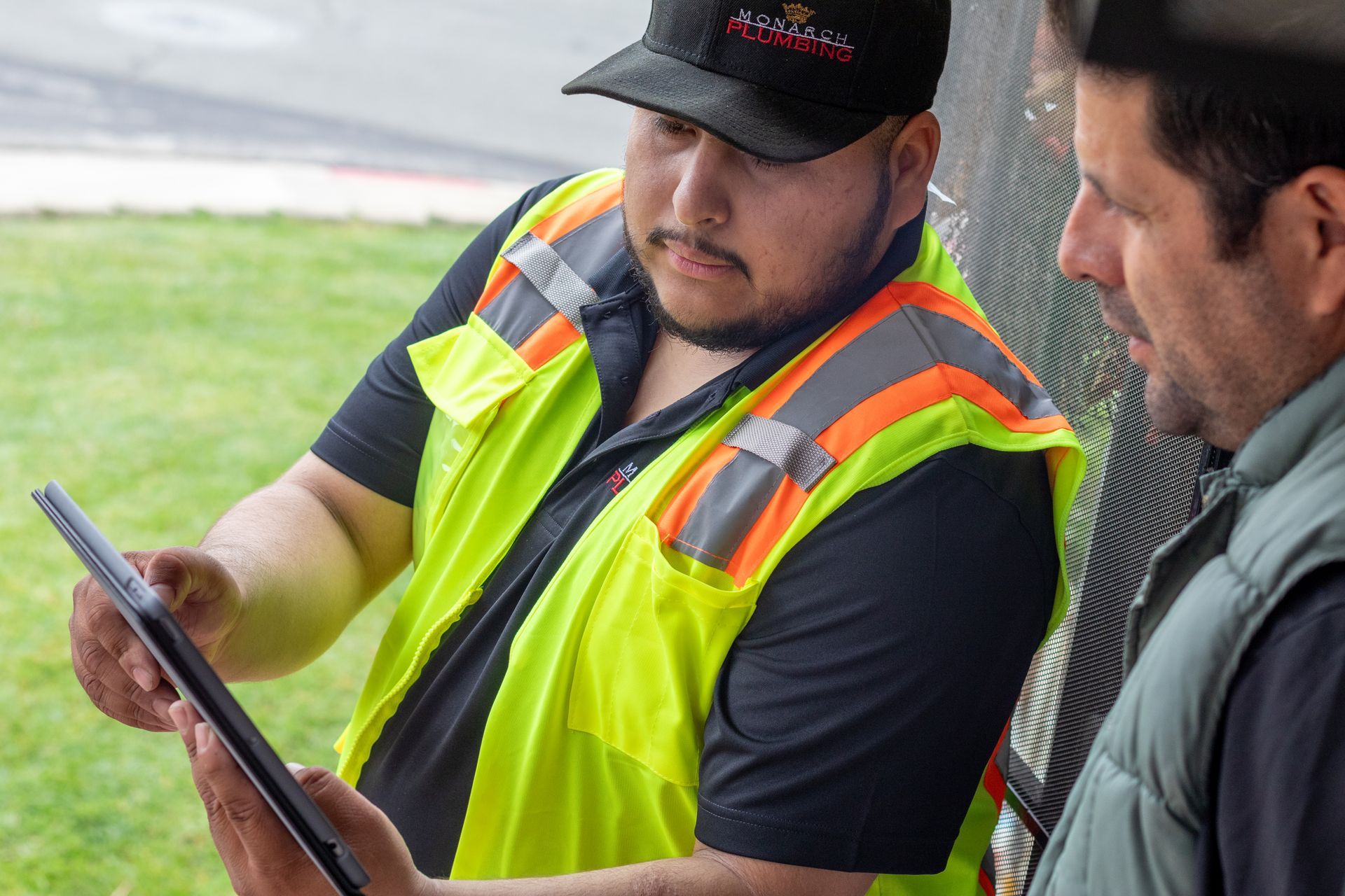 Two workers reviewing a tablet, one in a neon safety vest and hard hat, outdoors