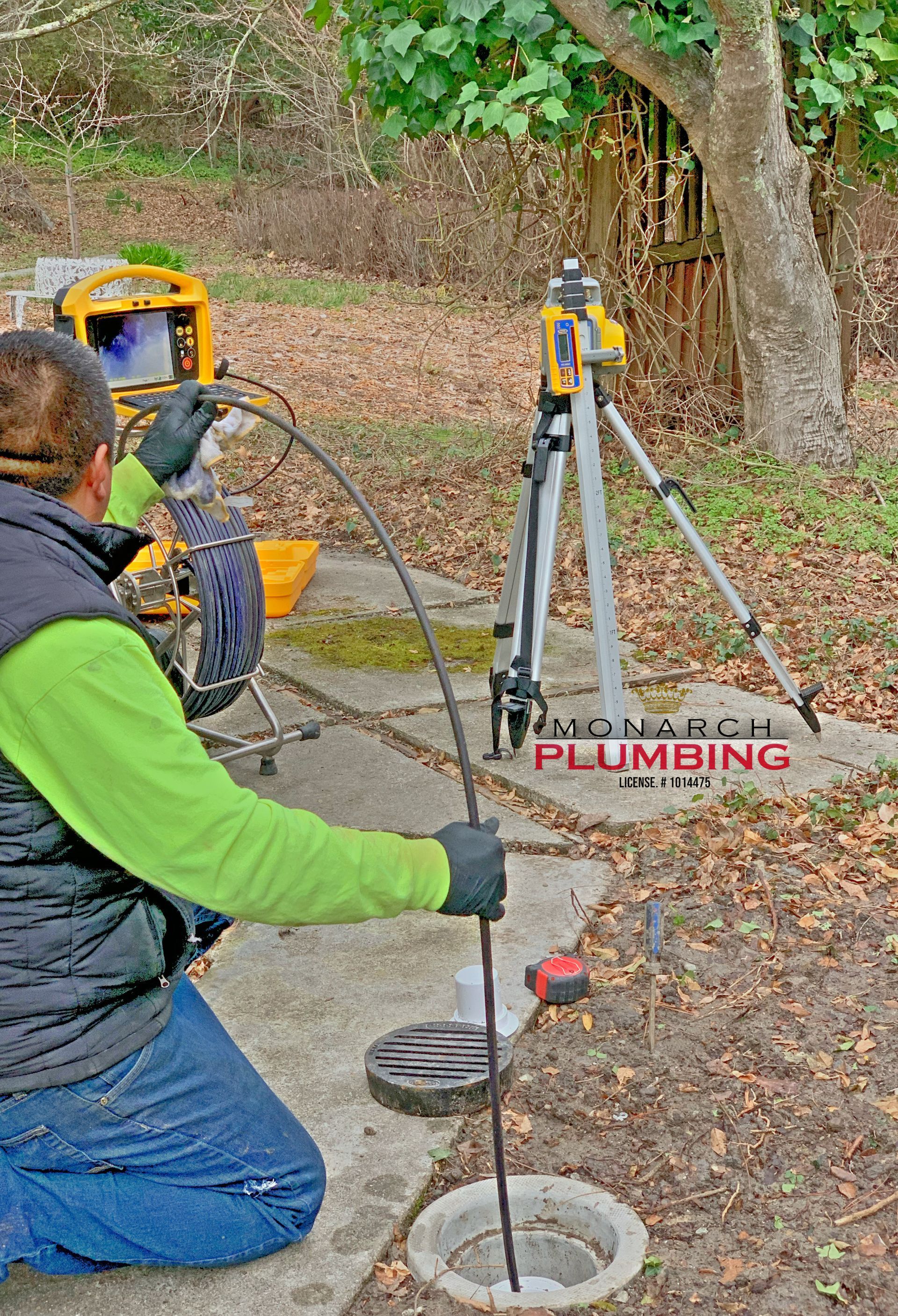 Technician using plumbing inspection equipment at an outdoor manhole in a wooded area