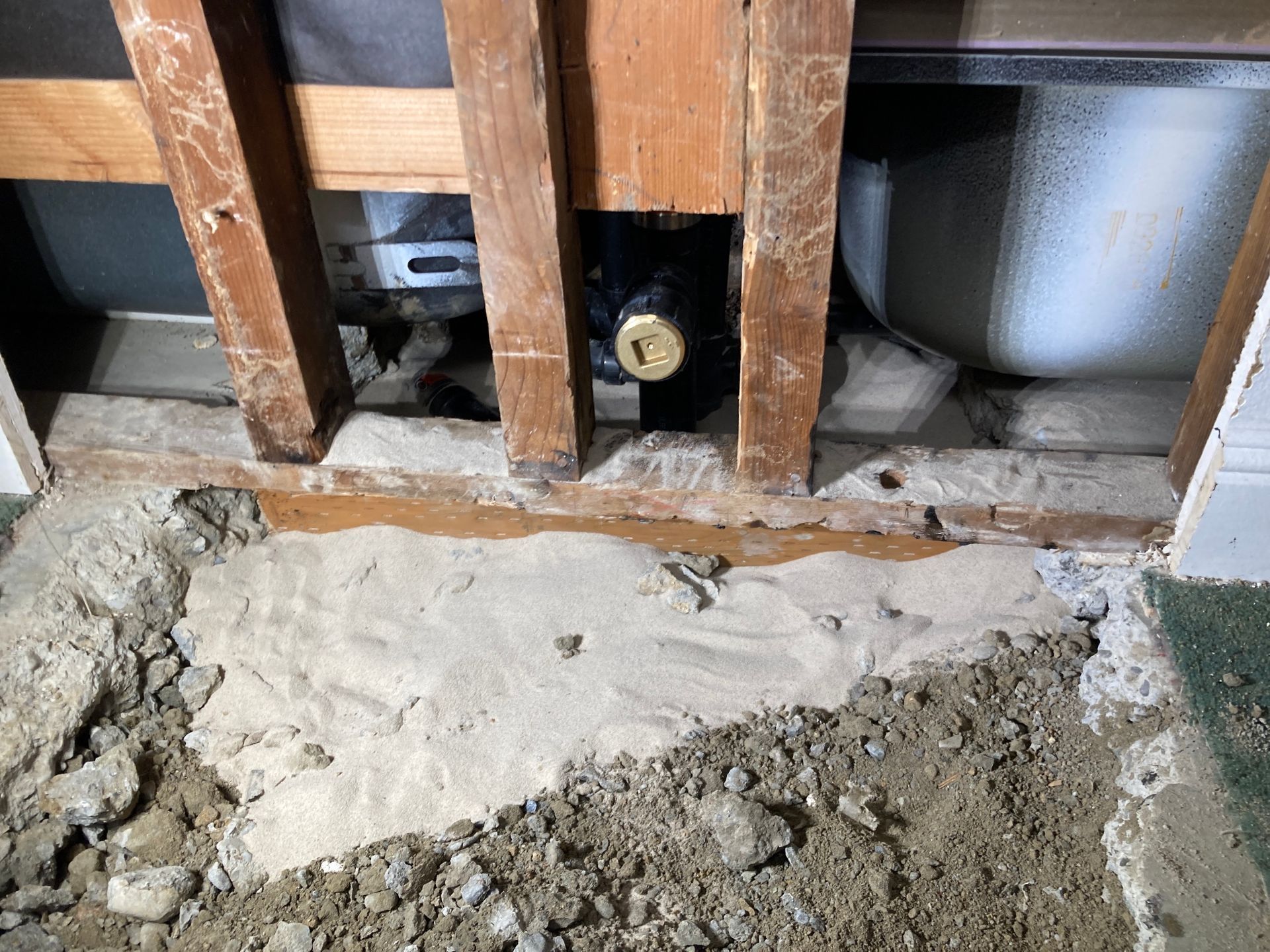 Exposed wall studs and plumbing behind a torn-out floor section