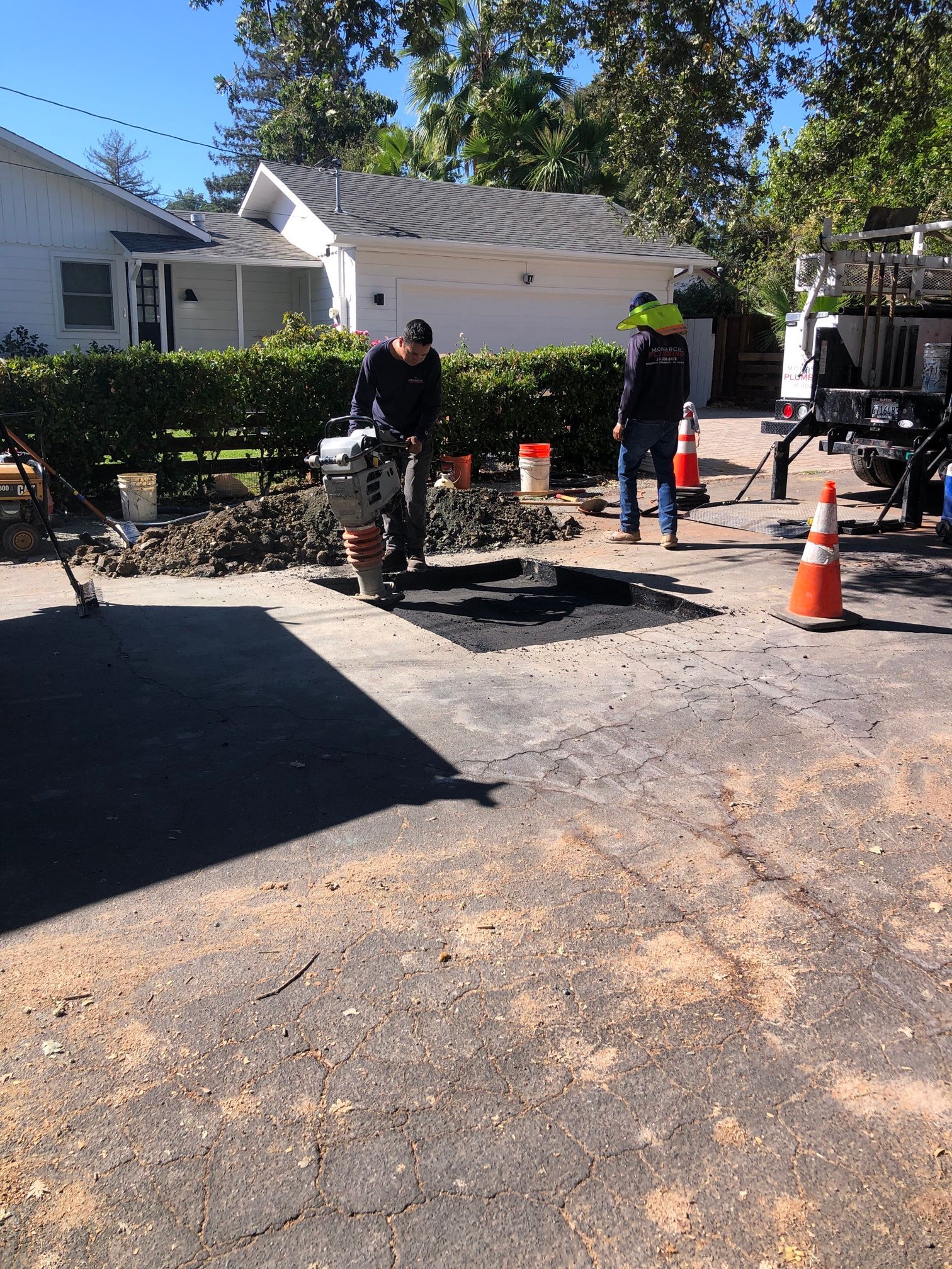 Workers prepping for sewer replacement, with one person using a jackhammer and orange traffic cones nearby.