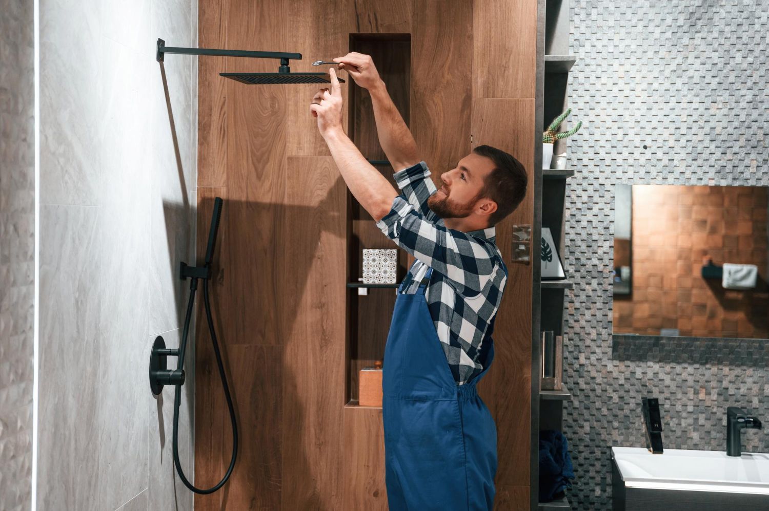 A man is fixing a shower head in a bathroom.