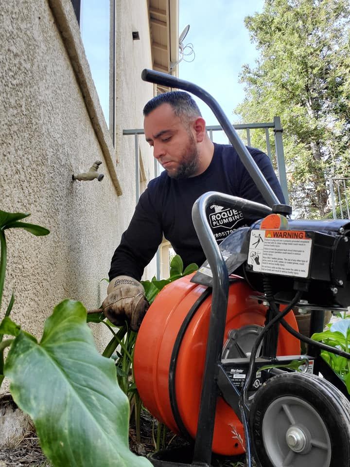 A man is using a machine to clean a drain outside of a building.