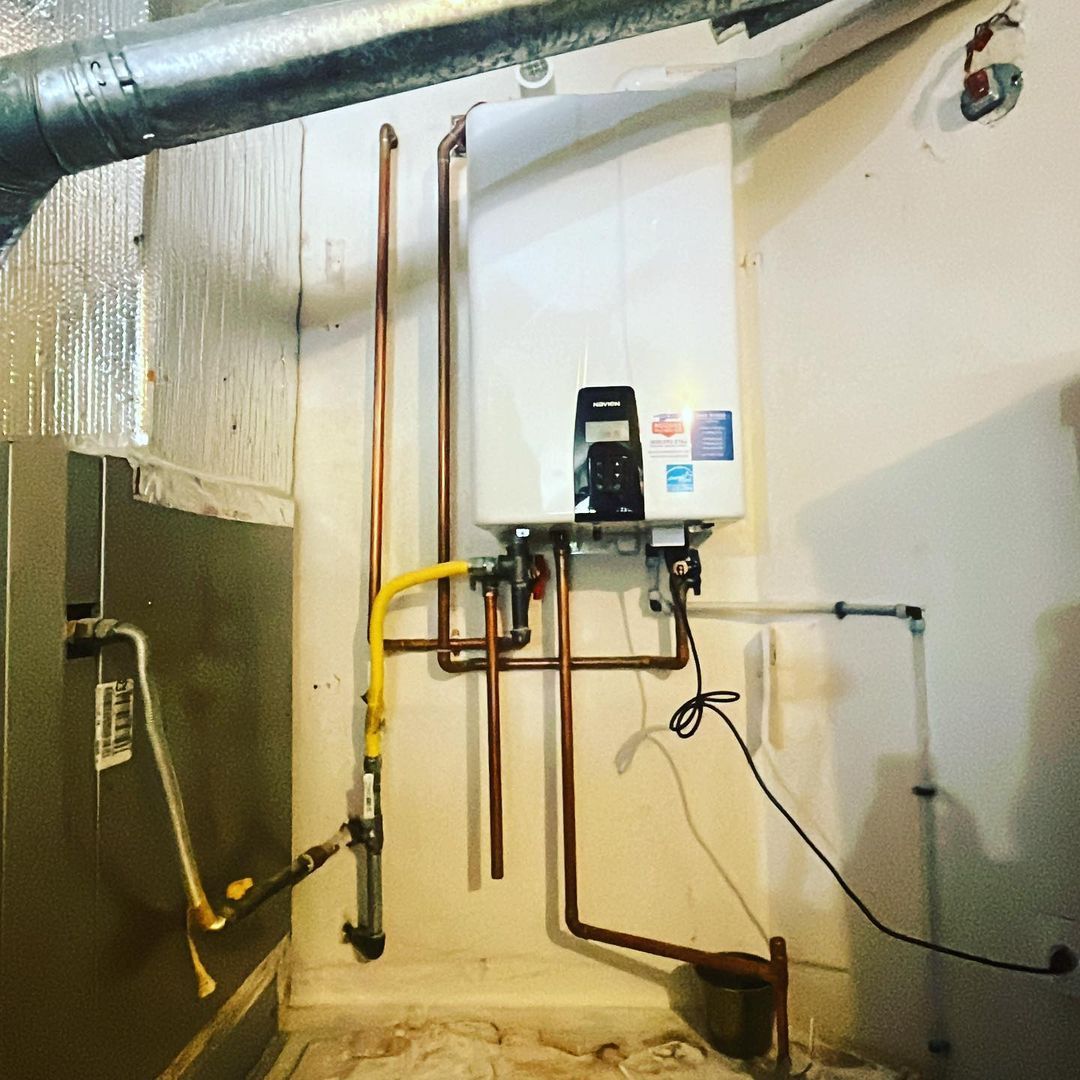 A room with a water heater and copper pipes on the wall.