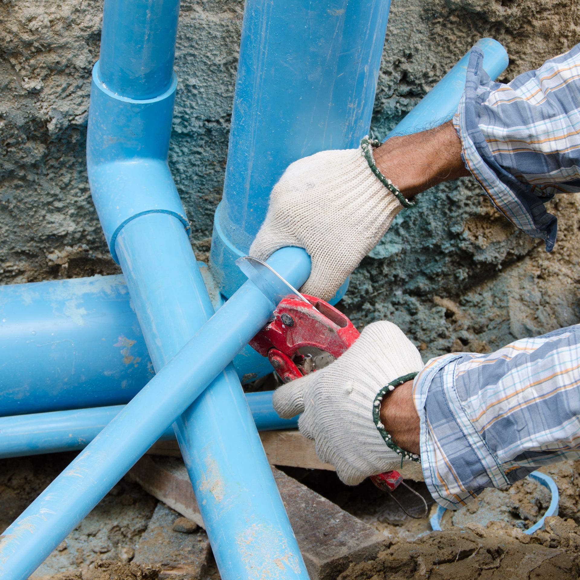 A man is cutting a blue pipe with a pair of scissors.