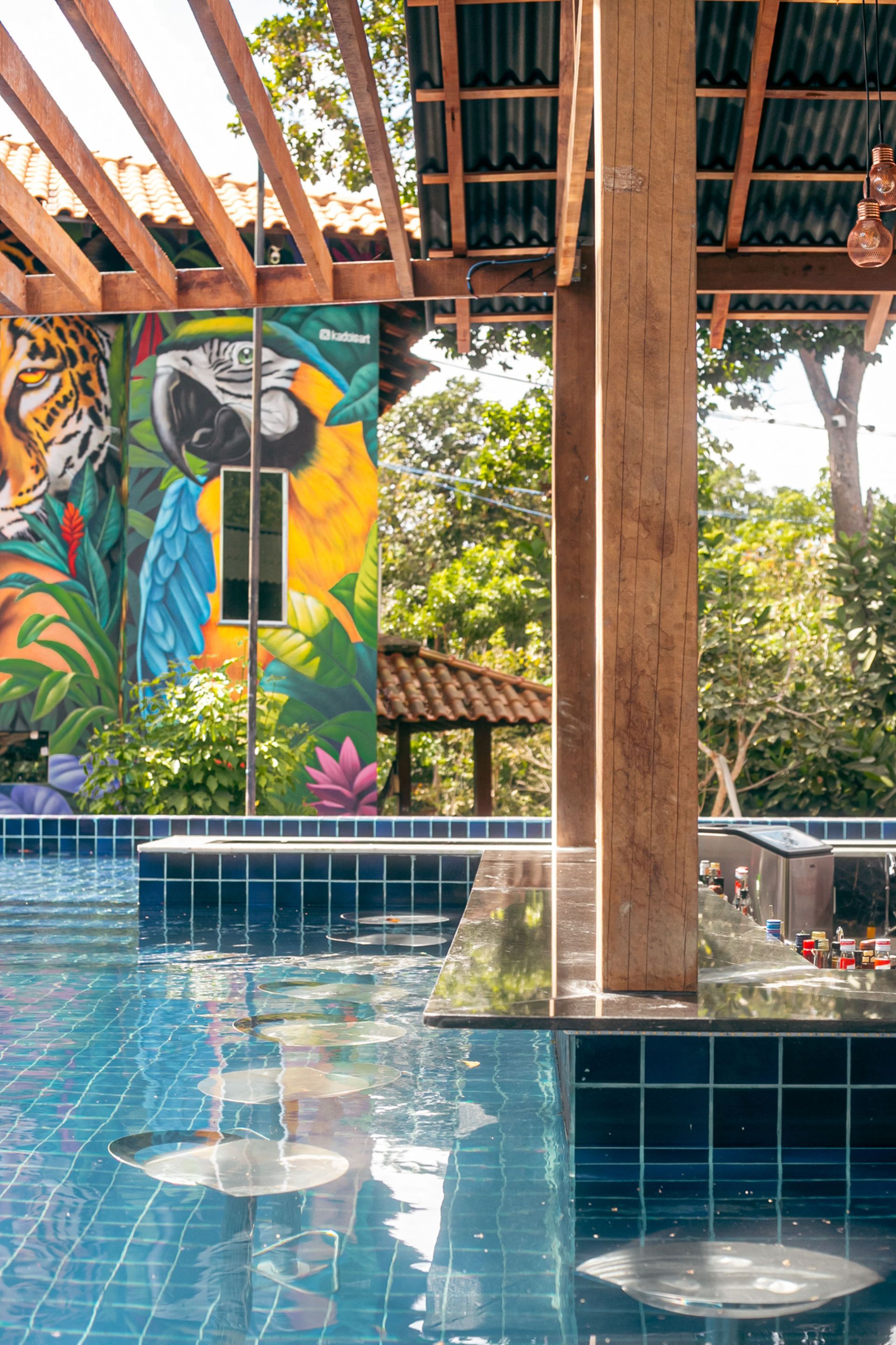Poolside mural with parrot and tiger, blue tile pool, wooden beams, tropical setting.