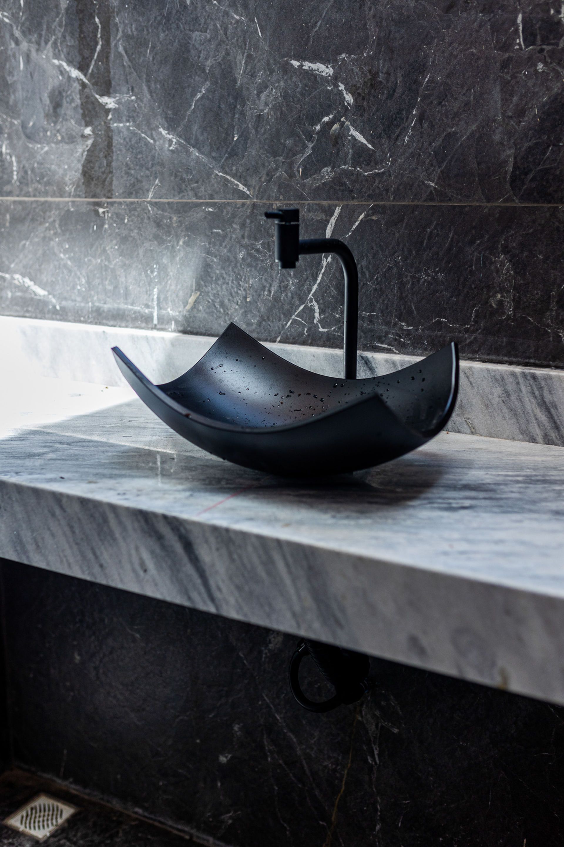 Black vessel sink on marble countertop, black faucet. Dark gray marble walls.