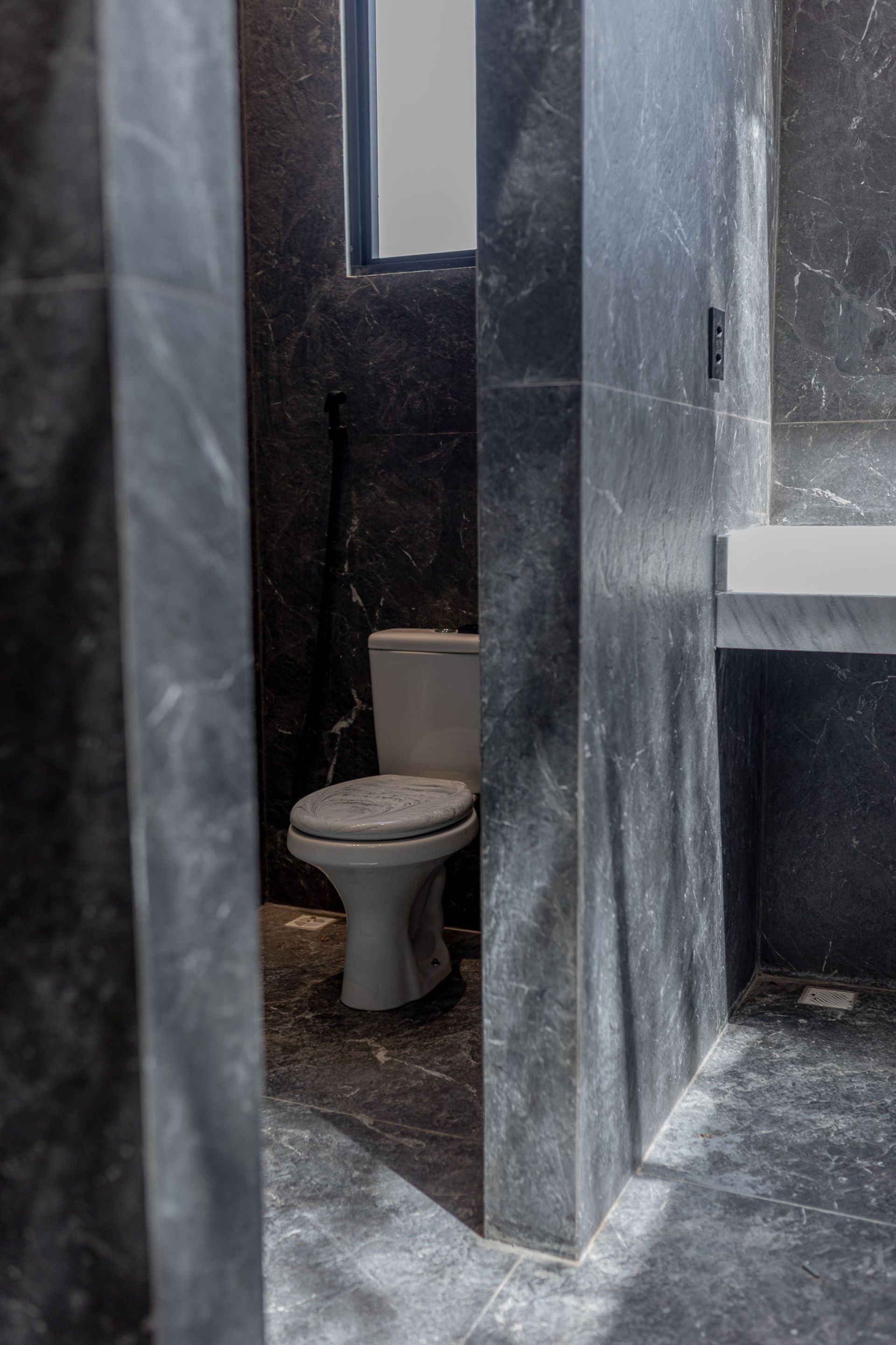 Bathroom with a white toilet and dark gray tiled walls.