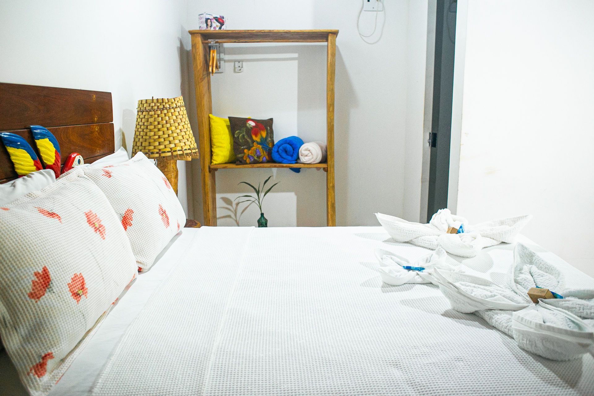 Bedroom with white bed, wooden headboard, and decorative pillows. A wooden clothes rack is in the background.