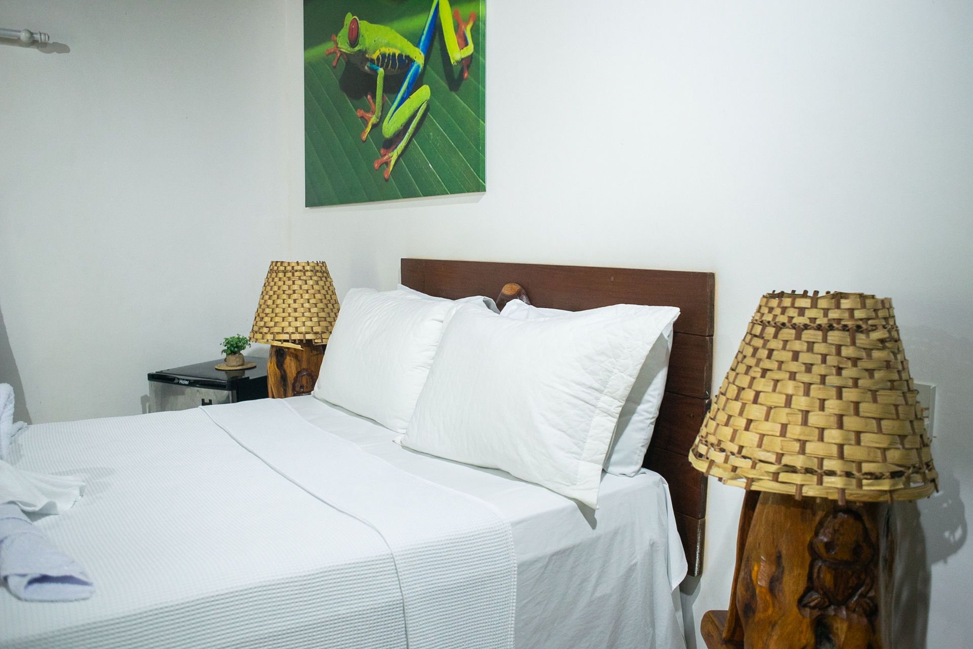 Bedroom with a white bed, two woven lamps, and a frog art print.