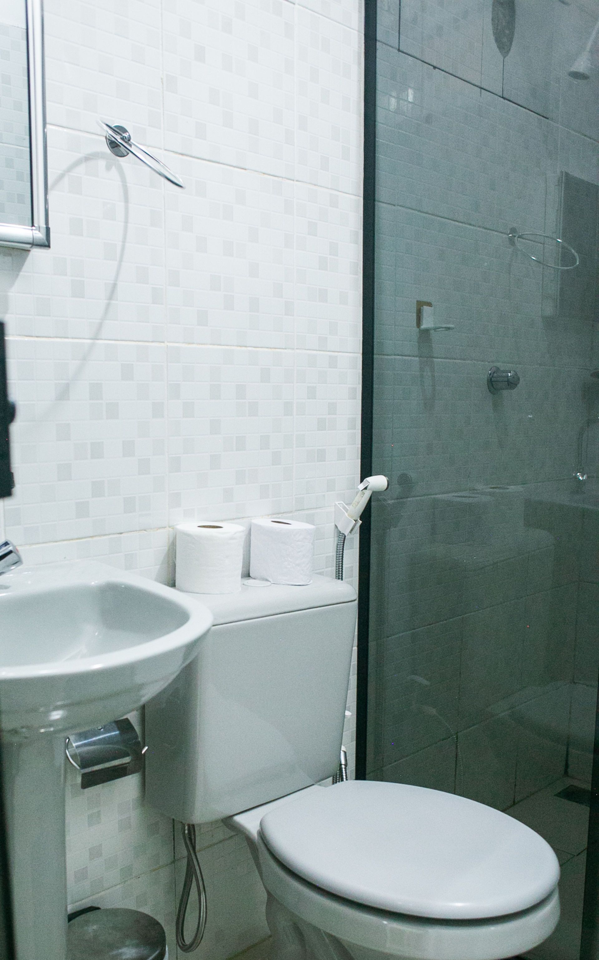 Bathroom with white fixtures, toilet, sink, and shower with glass door; white tile walls.