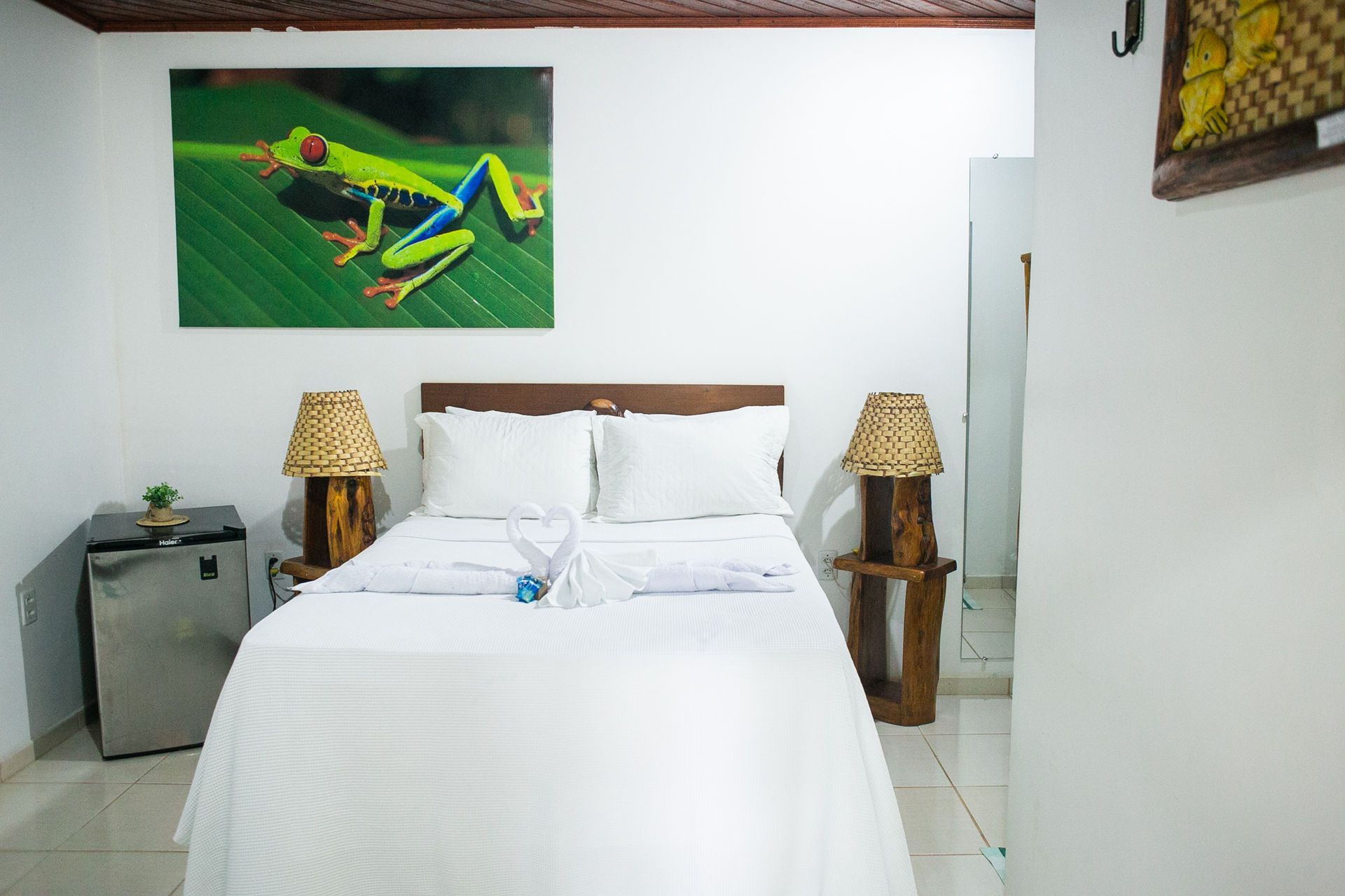 Bedroom with white bed, artwork of a green tree frog, and bamboo lamps.