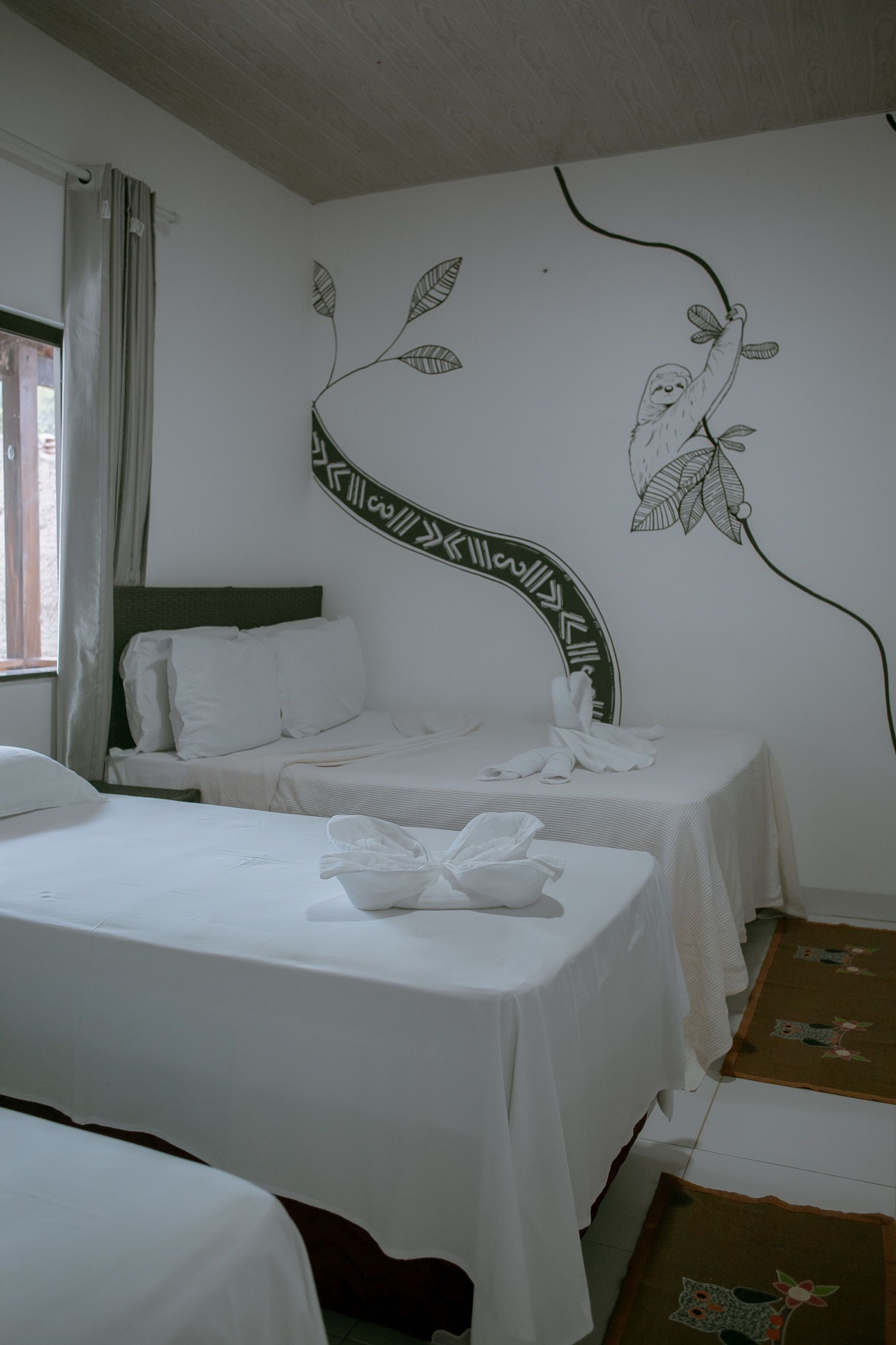 Three beds in a white room with a mural of a tree, and a curtain.
