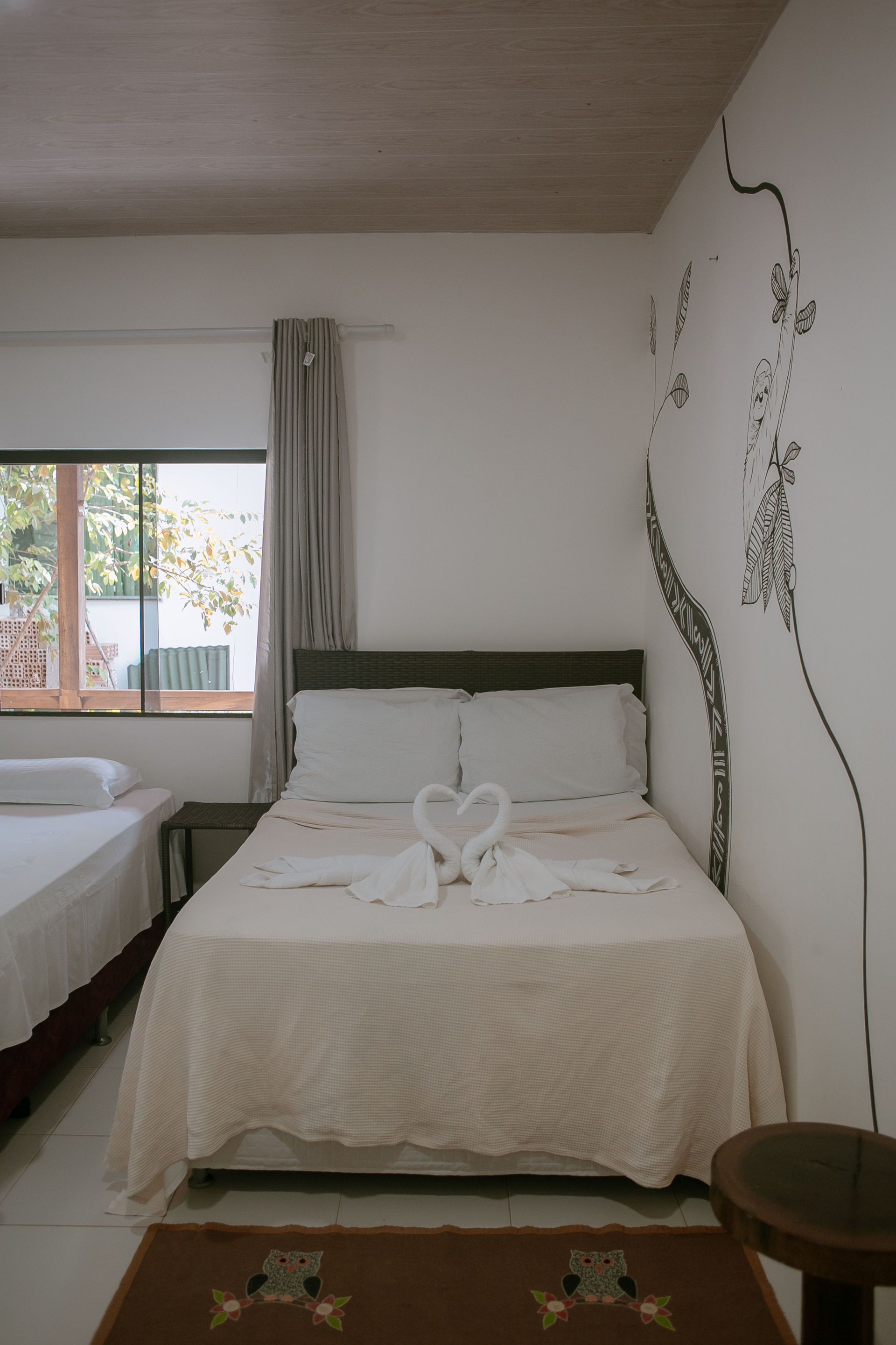 Bedroom with a bed adorned with towel swans, a window, a decorative wall design, and a side table.