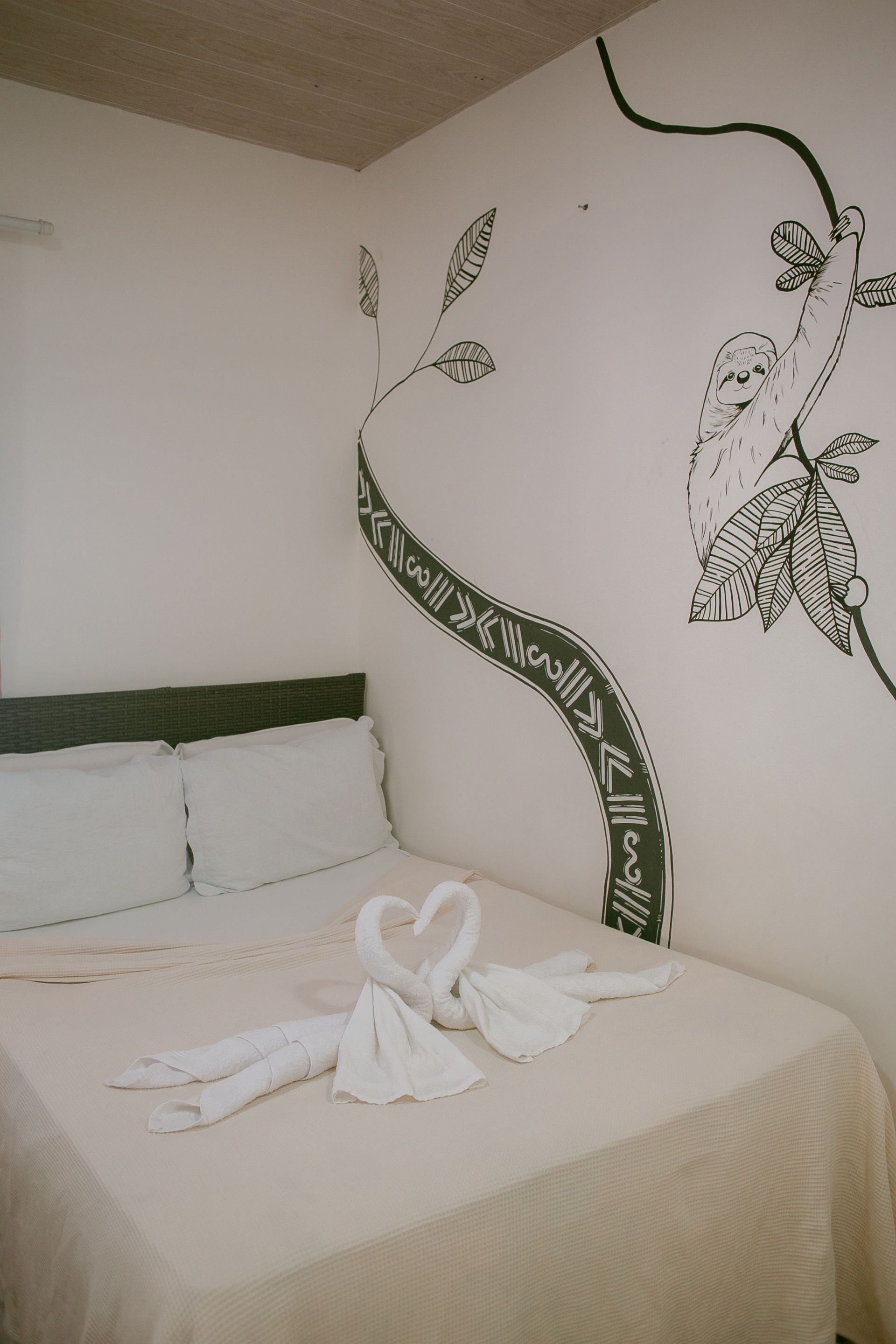 Bedroom with white walls, a bed decorated with towel swans, and a mural of a tree and monkey.