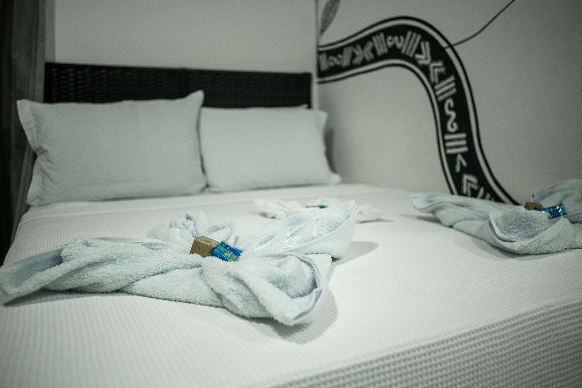 Bed with white linens, pillows, and folded blue towels; decorative wall art in the background.
