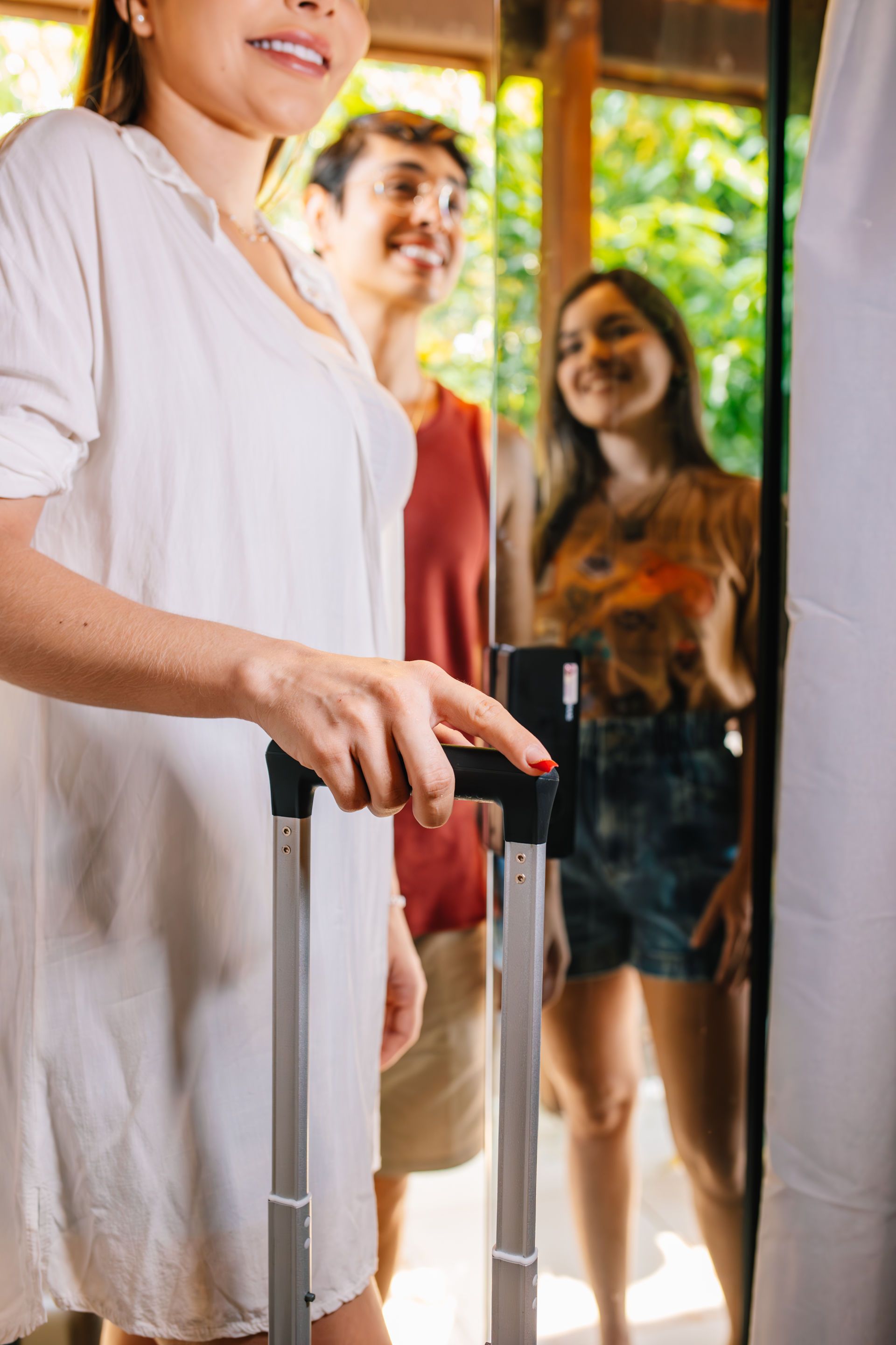 Woman with luggage, smiling, entering a doorway with two other smiling women in the background.