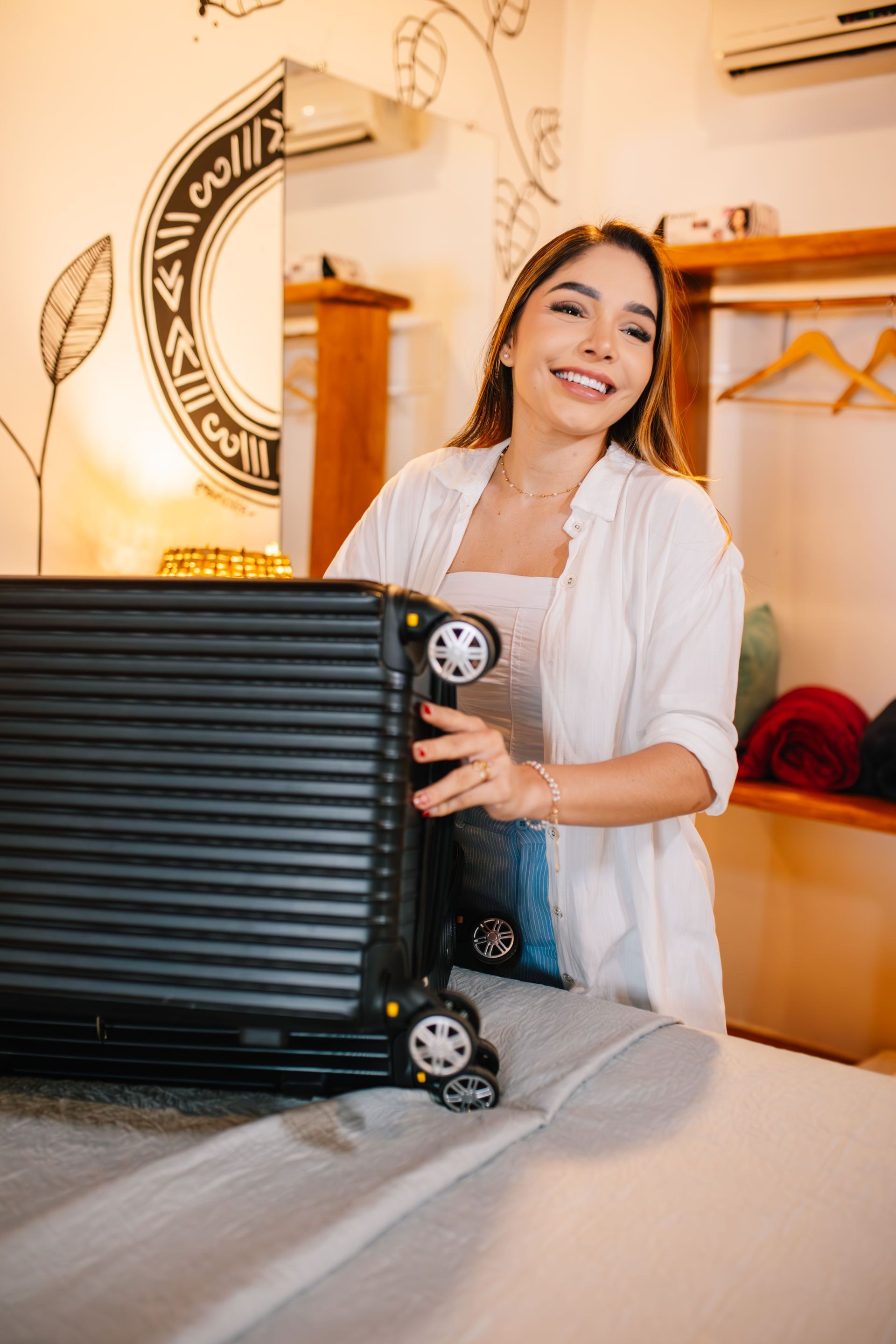Woman in white holding a black suitcase, smiling. Retail setting with art on wall.