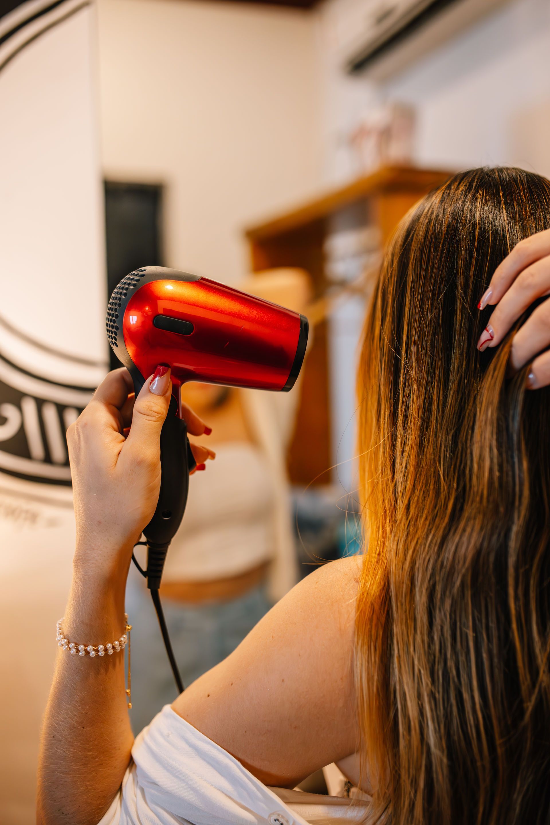 Woman drying her hair with a red hairdryer in front of a mirror.