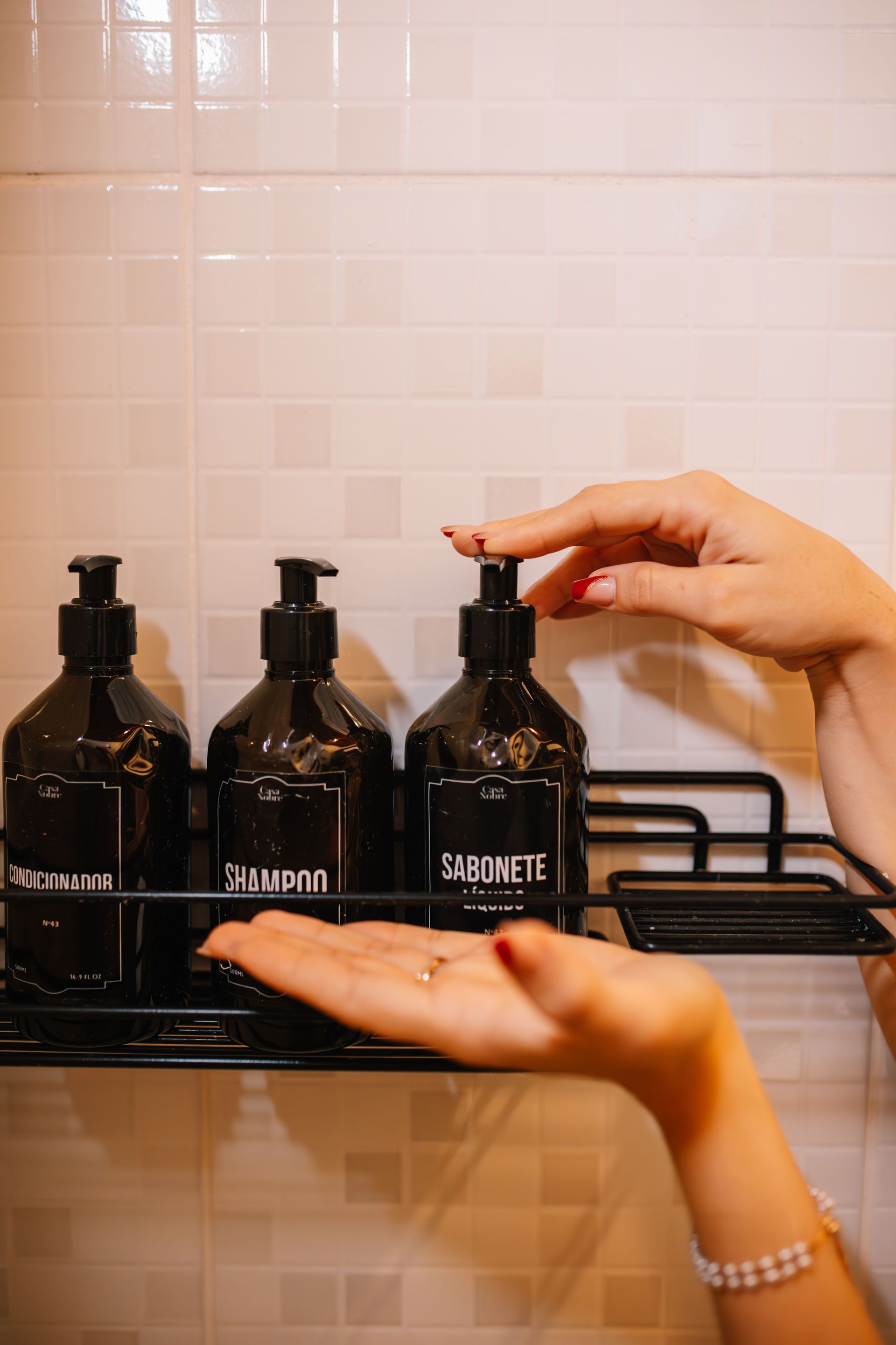 A person dispensing soap from a black bottle in a shower.