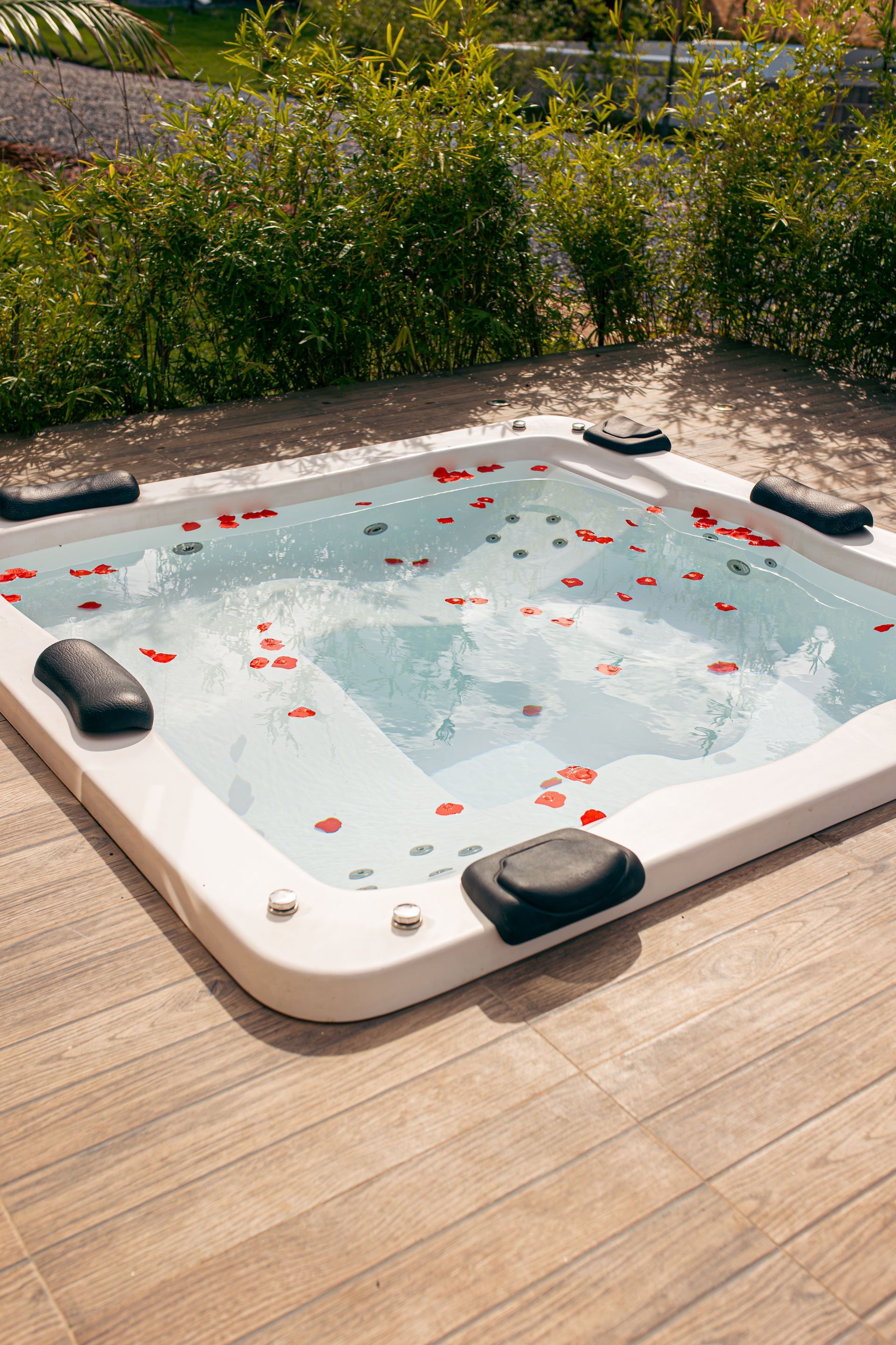 Hot tub filled with rose petals, set on a wooden deck, with greenery in the background.