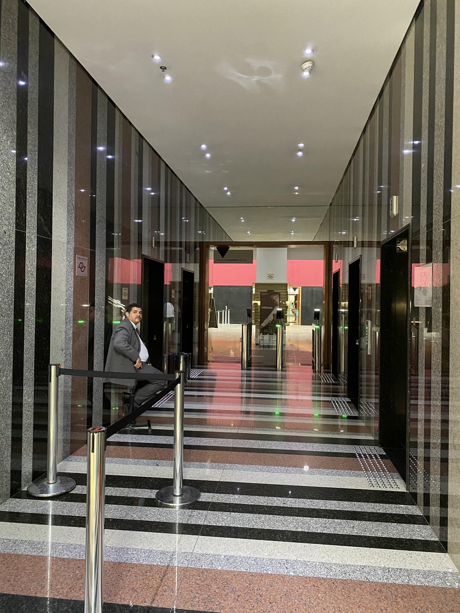 Um homem de terno está sentado em um longo corredor de um prédio.