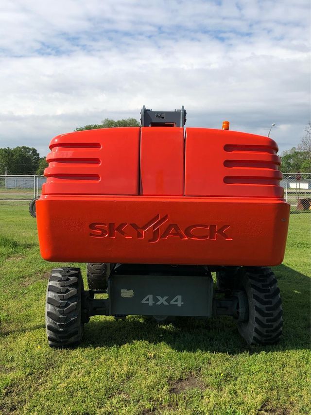 A red skyjack tractor is parked in a grassy field