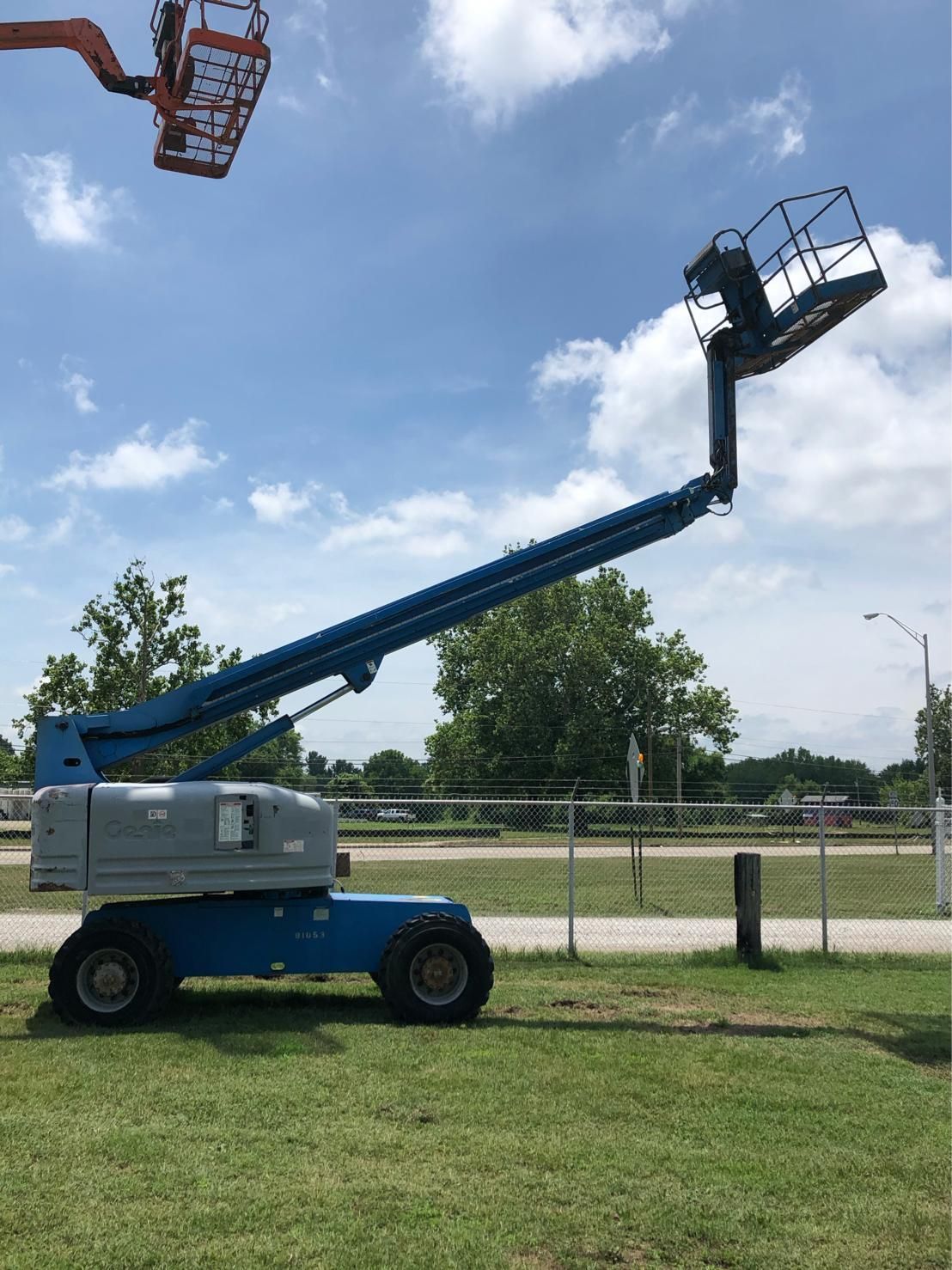 A blue aerial lift is sitting on top of a lush green field.