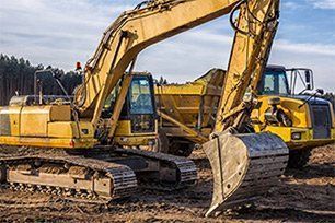 A couple of excavators are sitting on top of a dirt field.