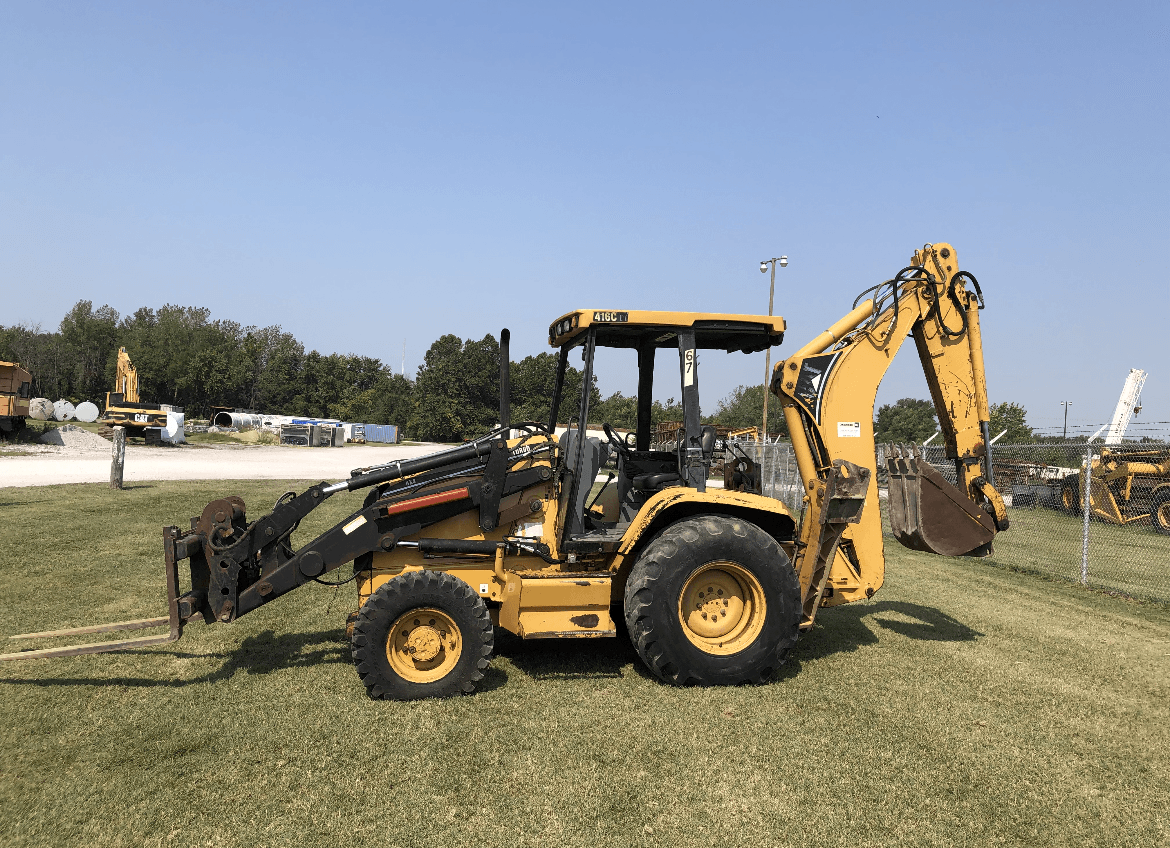 A yellow backhoe is parked in a grassy field.