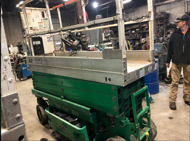 A man is standing next to a green scissor lift in a garage.