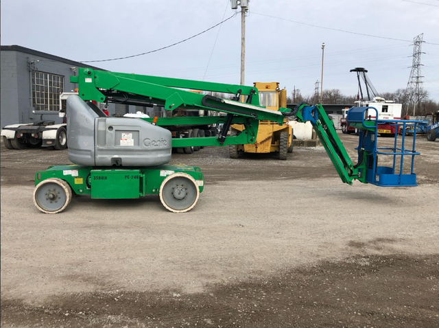 A green and gray aerial lift is parked in a parking lot.