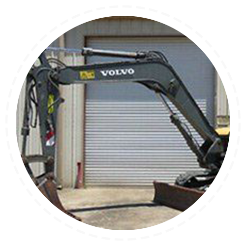 A volvo excavator is parked in front of a garage door.