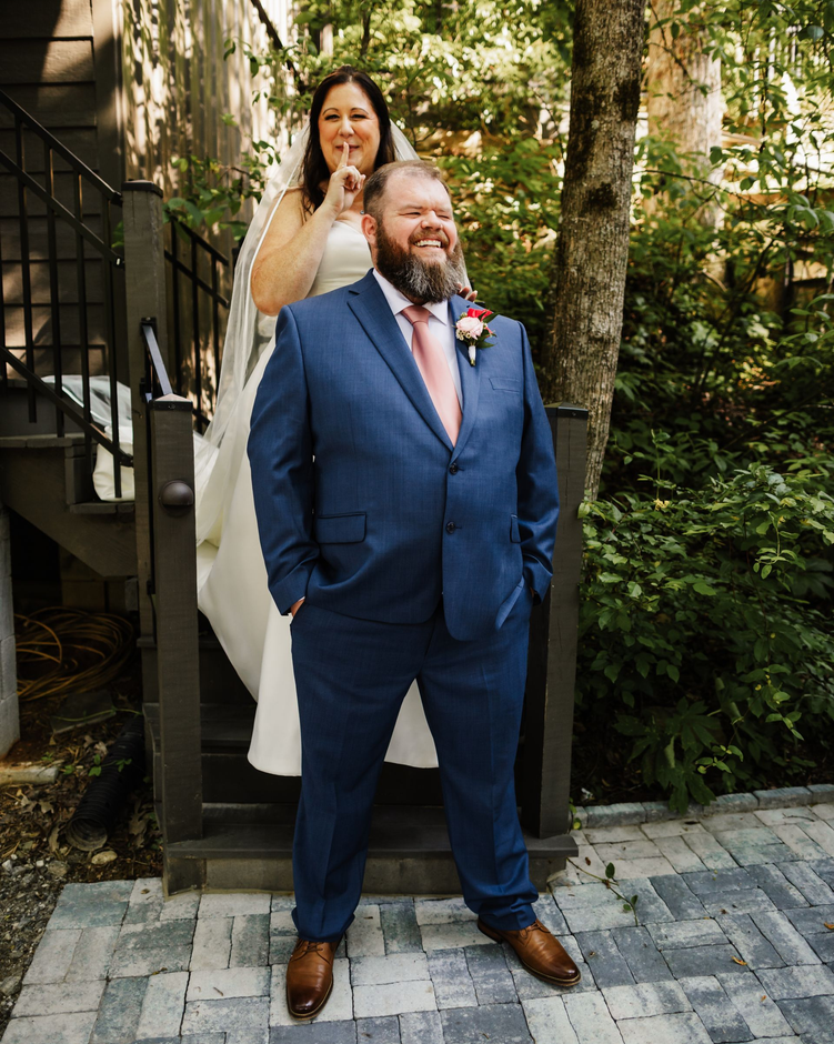 Wedding ceremony with couple, officiant, and guests in a forest setting under a decorated arch.