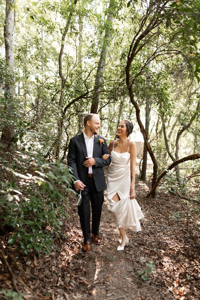 Bride in lace dress holds dried floral wreath. Sunny interior, arm tattoo.
