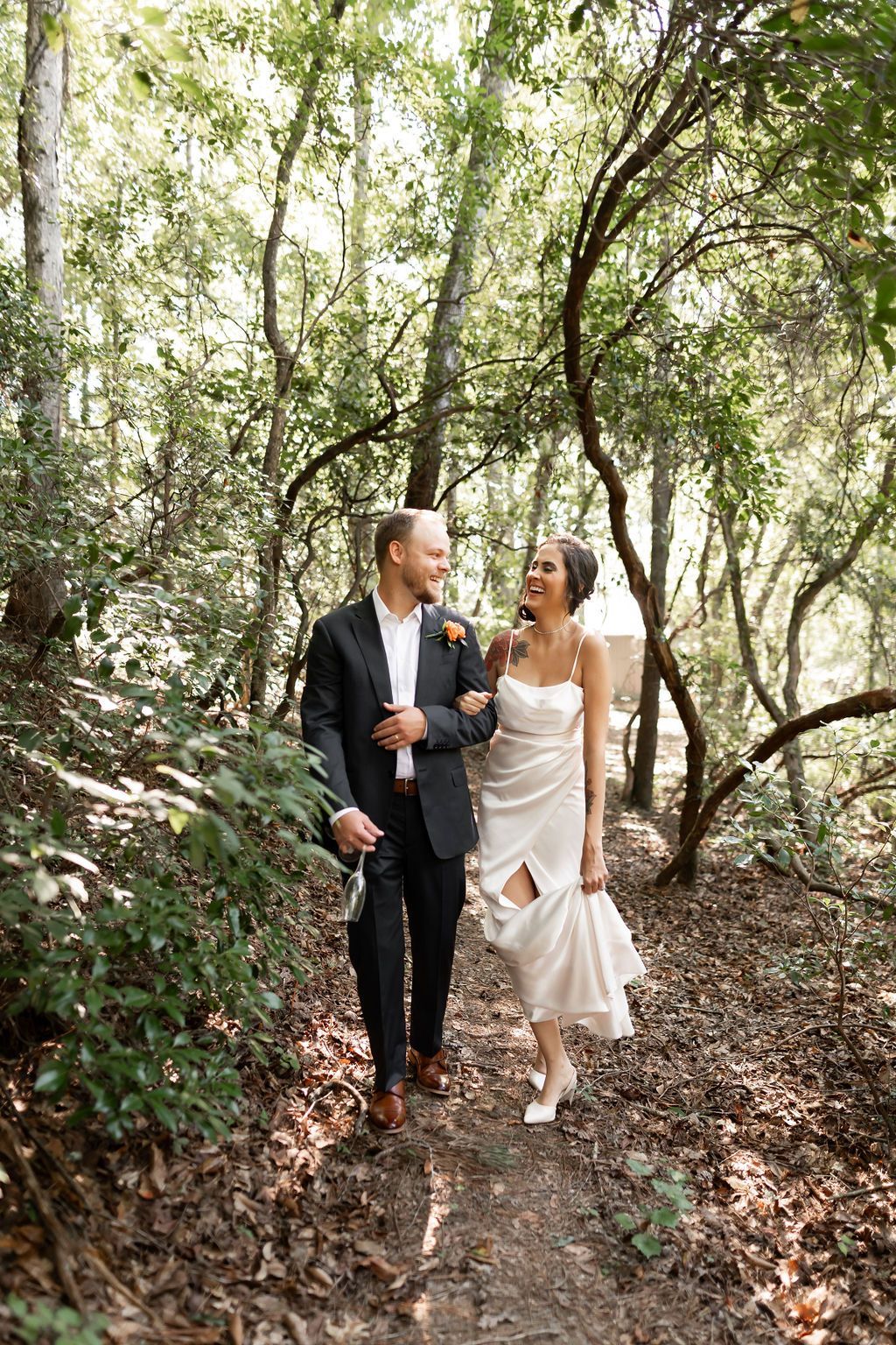 Bride in lace dress holds dried floral wreath. Sunny interior, arm tattoo.