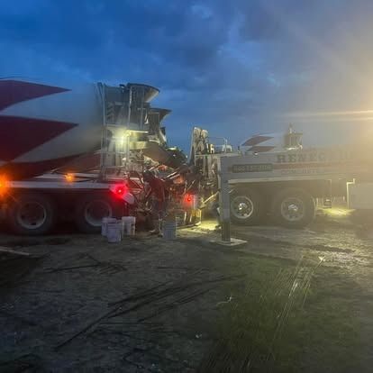 A concrete mixer truck is parked in a parking lot at night.