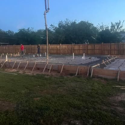 A concrete foundation is being poured in a backyard.