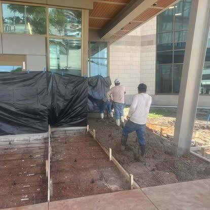 A group of construction workers are working on a sidewalk in front of a building.