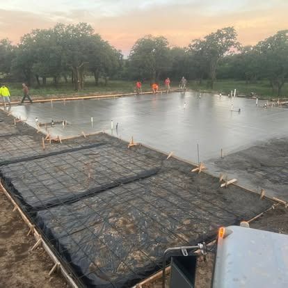 A concrete foundation is being built in a field with trees in the background.