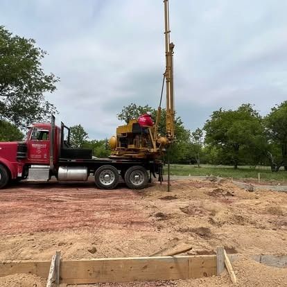 A red semi truck is parked in a dirt field next to a drill.