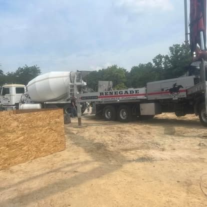 A concrete mixer truck is parked in a dirt lot next to a concrete pump truck.