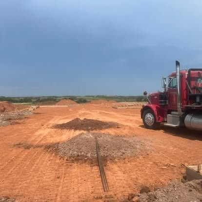 A red semi truck is parked in a dirt field.