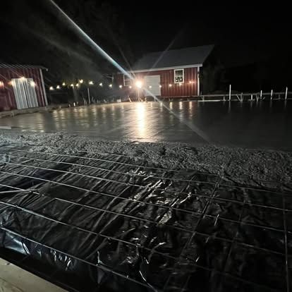 A black and white photo of a concrete driveway at night with a red barn in the background.