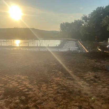 The sun is shining through the trees over a body of water.